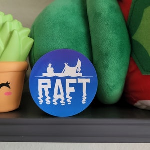 May include: A blue and purple round sticker with a white silhouette of a person in a raft with a tent and the word "RAFT" in white letters.