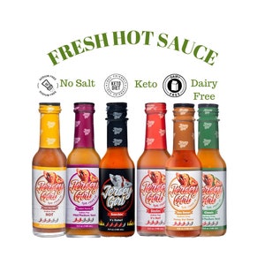 May include: Six glass bottles of Jersey Girl Hot Sauce in various flavors. The bottles are labeled with the flavor name, heat level, and ingredients. The bottles are arranged in a row on a white background. The labels are in a retro style with a pin-up girl design. The flavors are: Hot, Medium Heat, Scorchin', Sizzlin', Bon Bon, and Classic.