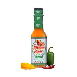 Puede incluir: Una botella de 148 ml de salsa picante Jersey Girl con una etiqueta verde y blanca que muestra a una mujer con un vestido rojo y un chile rojo. La etiqueta dice "Clásico" y "Sin sodio". La botella está sobre una superficie blanca con un pimiento verde y un chile rojo.