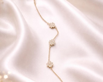 May include: A delicate gold bracelet featuring four clover-shaped charms, each adorned with sparkling crystals. The bracelet is displayed on a white satin background, creating a luxurious and elegant aesthetic. The bracelet's total length is approximately 7 inches.
