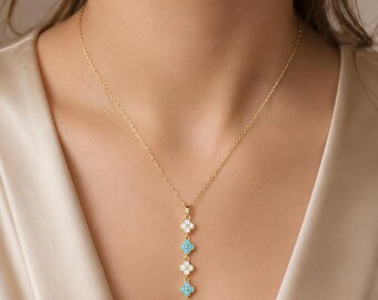 May include: A gold chain necklace featuring a vertical drop pendant composed of five alternating flower-shaped charms. Three charms are set with clear white stones, while two charms are set with bright turquoise blue stones in a linear arrangement.