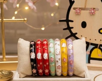 May include: A set of seven colorful bangles, each adorned with a cartoon character and floral accents. The bangles are displayed on a beige cushion inside a rectangular tray. Colors include black, red, green, white, yellow, and purple.