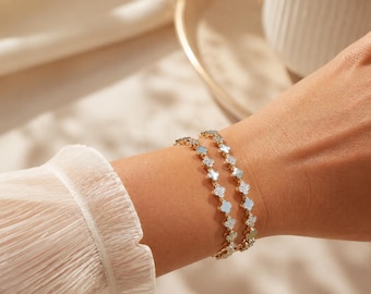 May include: Two gold-toned chain bracelets featuring a series of small, four-leaf clover-shaped charms. Each charm alternates between a smooth, iridescent white inlay and a sparkling, clear stone-encrusted surface, linked by a delicate gold chain.