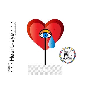 May include: A red heart with a blue eye and a teardrop, on a black stand. The heart is divided into sections numbered 1 through 9. The stand is on a grey wood base. The text "Arte Amalia Crafts" is on a circle with a colourful border.