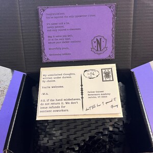 K&ouml;nnte beinhalten: Ge&ouml;ffnete schwarze Box mit einer lila Karte und einer Postkarte. Die lila Karte tr&auml;gt den Text "Gl&uuml;ckwunsch...Wednesday Addams". Die Postkarte tr&auml;gt den Text "Meine unaufgeforderten Gedanken...-W.A." und "Fellow Outcast Nevermore Academy Jericho, VT 00013."