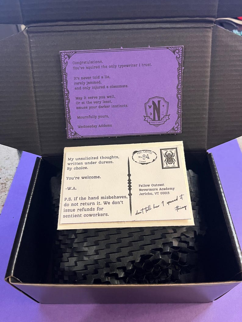 K&ouml;nnte beinhalten: Ge&ouml;ffnete schwarze Box mit einer lila Karte und einer Postkarte. Die lila Karte tr&auml;gt den Text "Gl&uuml;ckwunsch...Wednesday Addams". Die Postkarte tr&auml;gt den Text "Meine unaufgeforderten Gedanken...-W.A." und "Fellow Outcast Nevermore Academy Jericho, VT 00013."