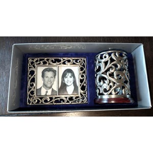 May include: A silver-toned picture frame with an ornate design, holding two black and white photos, is displayed next to a matching pen holder. The set is presented in a gift box with a blue velvet backing.
