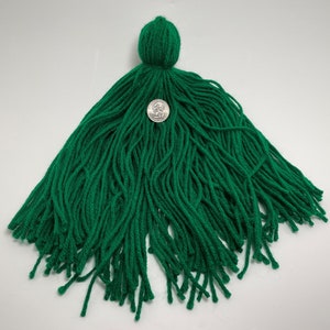 May include: A large green tassel with a round top. The tassel is made of yarn and is about the size of a US quarter.