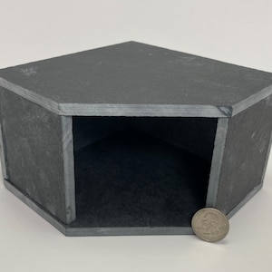 May include: A small, hexagonal, black slate house with a single opening. A US quarter is placed in front of the house for scale.