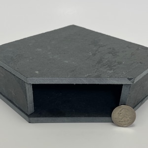 May include: A black slate corner shelf with a hexagonal shape. The shelf is about the size of a quarter.