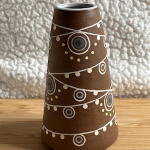 May include: A brown ceramic vase with a white glaze and a geometric pattern of circles and lines. The vase is decorated with yellow and blue accents.
