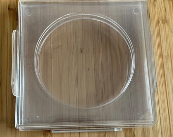 May include: A clear plastic square-shaped container with a round opening in the center. The container is designed to hold a round object, such as a candle or a soap.