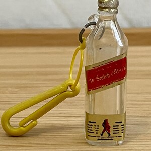 May include: A clear plastic miniature bottle keychain with a yellow plastic clip. The bottle has a label that reads "Old Scotch Whisky".