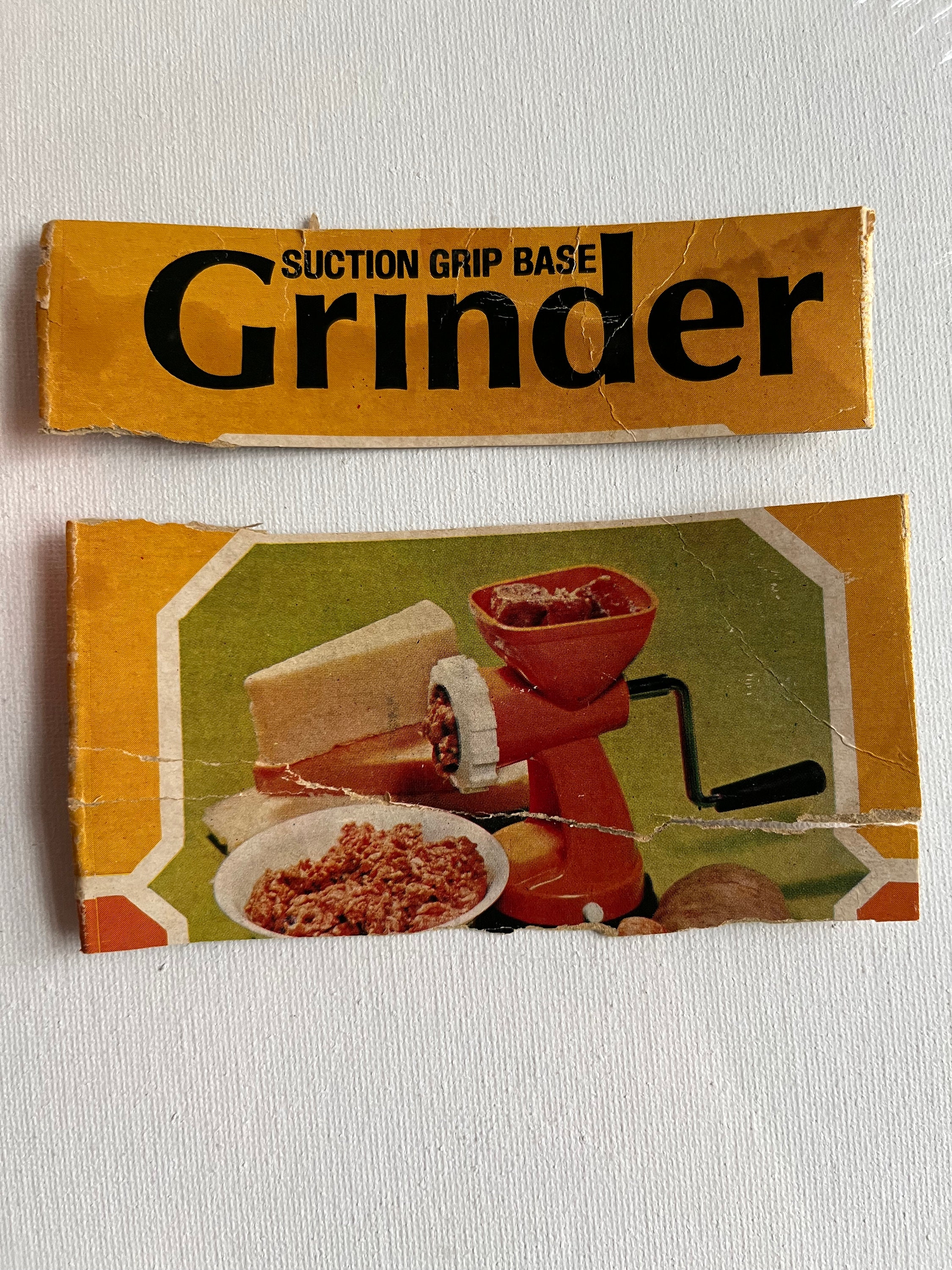 The image shows vintage packaging for a Hong Kong-style meat grinder with a bright orange color, featuring a picture of the machine and ground meat, and the words "Suction Grip Base Grinder."