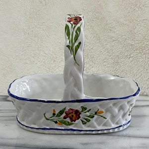 May include: White ceramic basket with a woven texture and a handle. The basket is decorated with red and yellow floral designs and a blue trim. The handle also features a floral design.