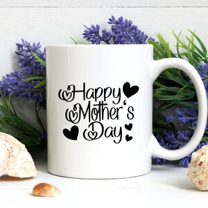 Puede incluir: Taza de cer&aacute;mica blanca con un dise&ntilde;o negro que dice "Feliz D&iacute;a de la Madre" con corazones alrededor del texto.
