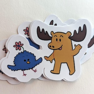 May include: A collection of die-cut stickers featuring cartoon animals. One sticker shows a blue bird with a pink flower, and another depicts a brown moose with large antlers. The stickers are white with colorful illustrations.