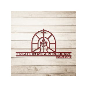 May include: A red metal wall art piece featuring a cross above praying hands within an arched window design. The text "CREATE IN ME A PURE HEART" and "PSALM 51:10" are below the window. The art is set against a light wood background.