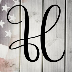 May include: Black cursive letter H on a white wood background with an American flag in the background.