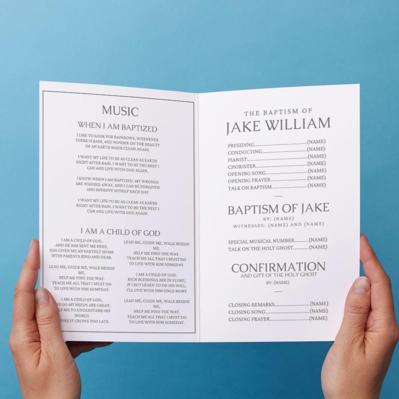 May include: An open booklet with the text "MUSIC" and "WHEN I AM BAPTIZED" on the left page, and "THE BAPTISM OF JAKE WILLIAM" on the right. The booklet is held open by two hands.