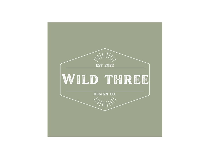 May include: A white logo on a sage green background. The logo is a hexagon with a starburst design at the top and bottom. The text inside the hexagon reads "WILD THREE DESIGN CO. EST 2022".