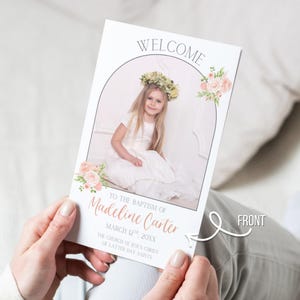 Pu&ograve; includere: Biglietto di annuncio battesimo tenuto da una persona. Il biglietto presenta una foto di una bambina con una corona floreale e un vestito bianco. Il testo include "WELCOME", "TO THE BAPTISM OF Madeline Carter" e la data. Accenti floreali adornano il biglietto.
