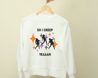 May include: An off-white crewneck sweatshirt featuring a graphic print of three black silhouettes of people dancing. The text "SO I CREEP" is printed above the figures and "YEAAAH" below, surrounded by orange, purple, and gray four-pointed stars.