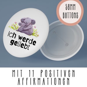 May include: A white button featuring a koala and baby koala embracing. The button reads "Ich werde geliebt" in black text. The button measures 58mm in diameter.