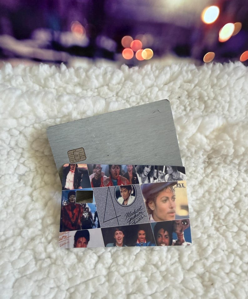 May include: A rectangular credit card featuring a collage of Michael Jackson images from the Thriller era. The design includes the number 40, the text Michael Jackson Thriller, and the P.Y.T. logo. The card has a metallic silver finish and a chip.