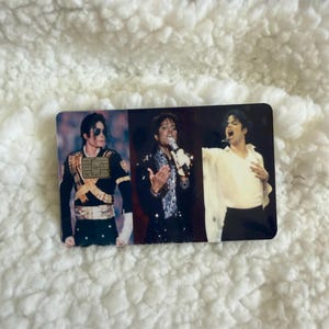 May include: A rectangular payment card featuring three distinct photographic images of Michael Jackson. The left image shows him in a military-style jacket, the center in a sequined shirt with a microphone, and the right in a white shirt.