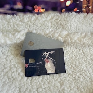 May include: A rectangular credit card featuring a printed image of a performer wearing a black sequined jacket, a white shirt, and a black fedora hat. The card has a small square cutout on the left side and a metallic chip embedded on the top surface.