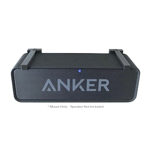 May include: A black speaker mount with the brand name "ANKER" in light gray lettering. The mount has a rectangular shape with a mesh front and a blue power indicator light. The text "Mount Only - Speaker Not Included" is below the speaker.