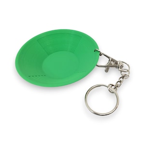 May include: A bright green miniature gold pan keychain. The small, round pan has a ridged interior and is attached to a silver-colored clasp and key ring. The keychain is designed to be a novelty item.