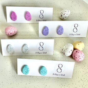 May include: A set of six pairs of handmade polymer clay earrings shaped like speckled eggs. The earrings are displayed on white cards with the text "8 Clays a Week".