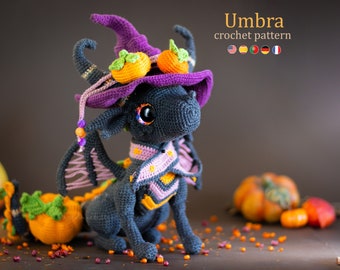 May include: A crocheted black dragon wearing a purple witch hat with orange pumpkins. The dragon has a pink and orange scarf and wings. The dragon is sitting on a brown surface with orange and brown pumpkins.