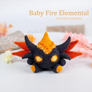 May include: A crocheted Baby Fire Elemental doll with a dark gray body, orange accents, and yellow eyes. The doll has a spiky orange crown and wings. The text "Baby Fire Elemental crochet pattern" is in the image.