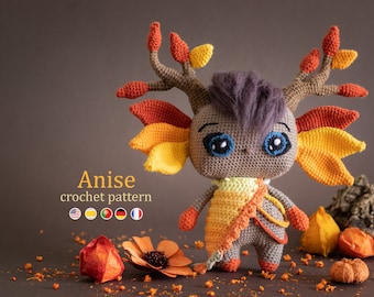 May include: A crocheted doll with a whimsical design. The doll has large blue eyes, a purple hair tuft, and brown antlers with orange and yellow leaves. It wears a yellow and orange shawl. The text "Anise crochet pattern" is visible.