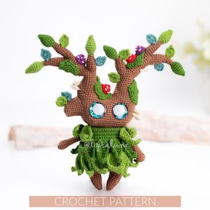 May include: A handmade crochet doll resembling a tree-like creature. The doll has a brown body, green leaves, and branches with colorful accents. The doll has large, sparkling blue eyes and a green skirt. The text "CROCHET PATTERN" is at the bottom.