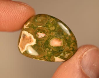 May include: A polished, rounded stone featuring a mottled pattern of deep forest green, olive, and cream-colored inclusions. The surface has a smooth, glossy finish with distinct circular and irregular shapes embedded throughout the mineral structure.