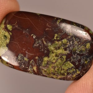 Könnte beinhalten: Ein glatter, polierter, grüner und brauner Edelstein-Cabochon mit einem einzigartigen Muster. Der Stein hat eine rotbraune Basis mit grünen und schwarzen Einschlüssen.