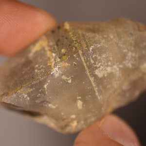 May include: A clear, faceted crystal with a rough, natural texture. The crystal has a light brown colour and is covered in small, white inclusions.