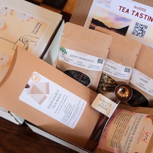 May include: A brown box filled with a tea tasting kit. The kit includes four different types of tea, a tea spoon, and disposable tea bags. The box also includes a card with instructions for a guided tea tasting experience.