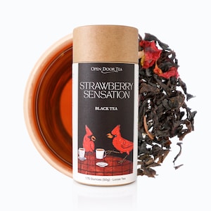 May include: A brown cardboard tube with a label that reads "Open Door Tea Strawberry Sensation Black Tea". The label features a red cardinal illustration and the text "1.75 Ounces (50g) - Loose Tea".