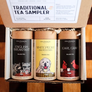 May include: A brown cardboard box with a white label that reads "TRADITIONAL TEA SAMPLER" and contains three brown tubes of loose leaf tea. The tubes are labeled "English Breakfast", "White Peony - Bai Mou Dan", and "Earl Grey". Each tube features a cartoon illustration of an animal and a teacup.