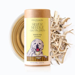 May include: A brown cardboard tube with a yellow label featuring a cartoon dog holding a cup of tea. The label reads "Open Door Tea, Silver Needle - Bai Yin Zhen - White Tea Reserve, 1 Ounces (28g) Loose Tea".
