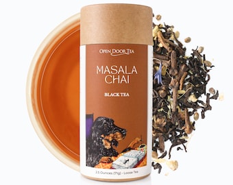 May include: A brown cardboard tube with a label that reads "OPEN DOOR TEA MASALA CHAI BLACK TEA 2.5 Ounces (71g) Loose Tea". The label features a cartoon illustration of a black dog sitting at a table with a book and a pen. A pile of loose leaf tea is scattered around the tube.