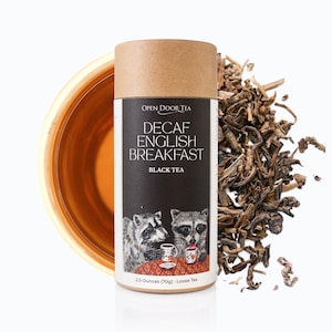 May include: A brown cardboard tube with a white label that says "Open Door Tea Decaf English Breakfast Black Tea". The label also features two raccoons drinking tea and the text "2.5 Ounces (70g) - Loose Tea".