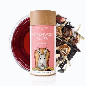 May include: A brown cardboard tube with a pink label that says "Open Door Tea Strawberry Glow Fruity Tea". The label features a cartoon rabbit sitting in a chair and drinking tea. The tube contains 1.75 ounces (50g) of loose leaf tea.