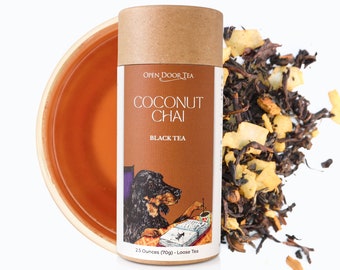 May include: A brown cardboard tube with a label that reads "OPEN DOOR TEA COCONUT CHAI BLACK TEA" and a cartoon illustration of a dog reading a book. The label also says "2.5 Ounces (70g) Loose Tea". A pile of loose leaf tea with coconut flakes is scattered around the tube.