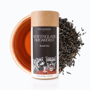May include: A brown cardboard tube with a black and white label that says "Open Door Tea New England Breakfast Black Tea". The label features an illustration of two raccoons drinking tea. The tube contains 2 ounces (57g) of loose leaf tea.